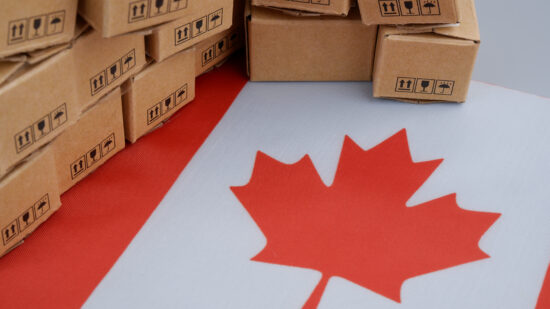 Canadian industry concept. Flag of Canada and many shipping carton boxes close-up.