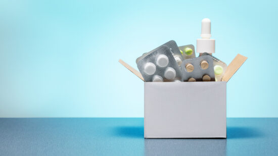 Cardboard box with different medicine pills, tablets and capsules on a blue background with copy space. Buying drug delivery concept.